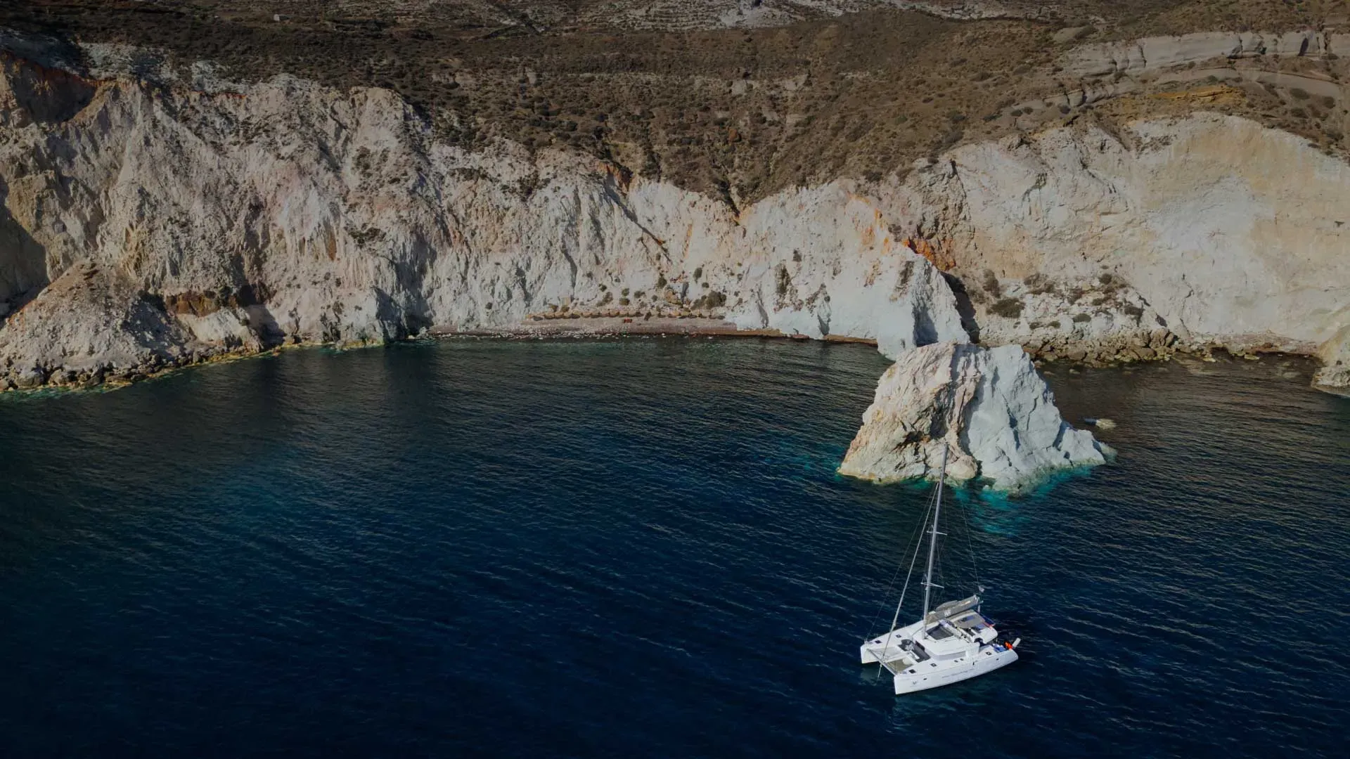 Private catamaran anchored below the white cliffs of Santorini