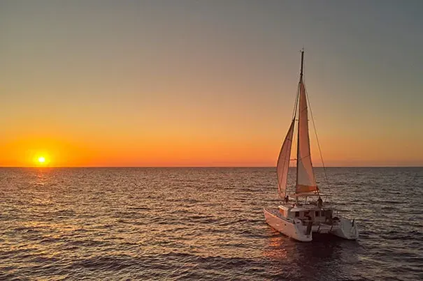 Catamaran sailing cruising Red & White Beach during golden hour