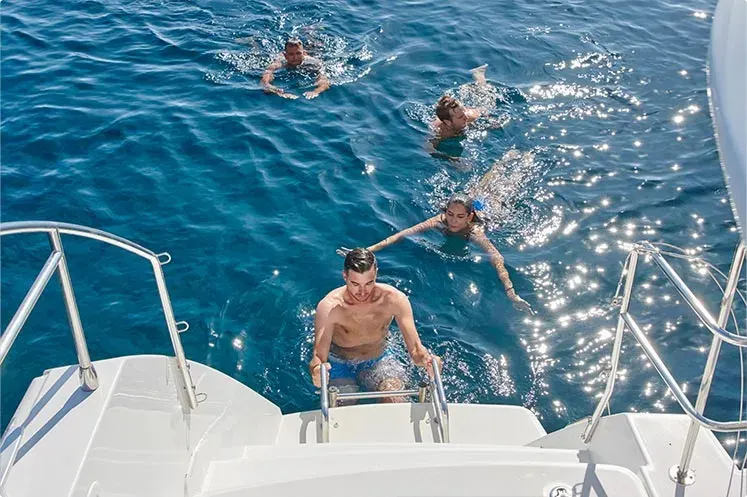 Small group snorkelling in crystal‑clear Aegean Sea beside the anchored catamaran