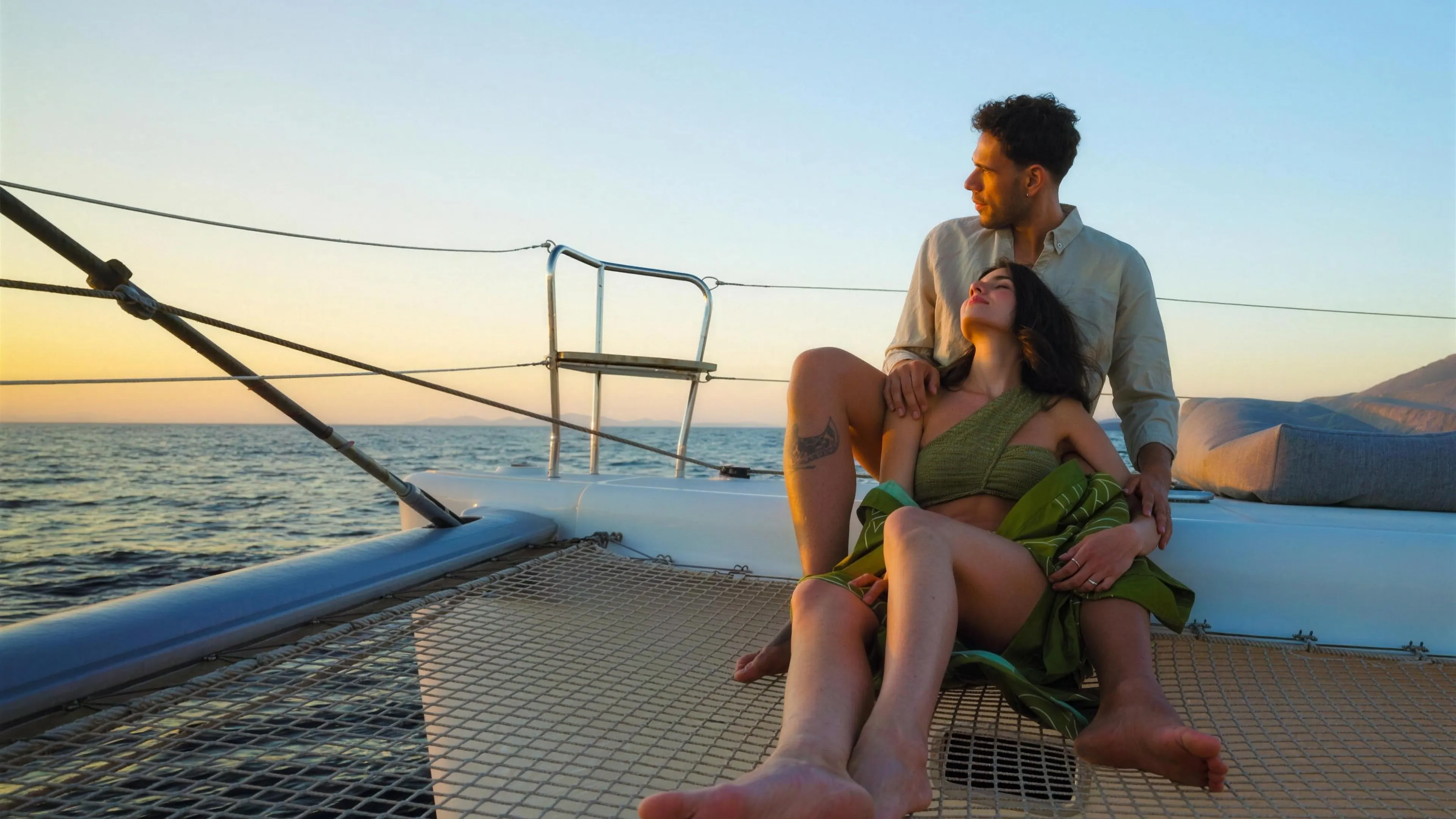 Couple on the catamaran net in the golden light of a Santorini sunset cruise