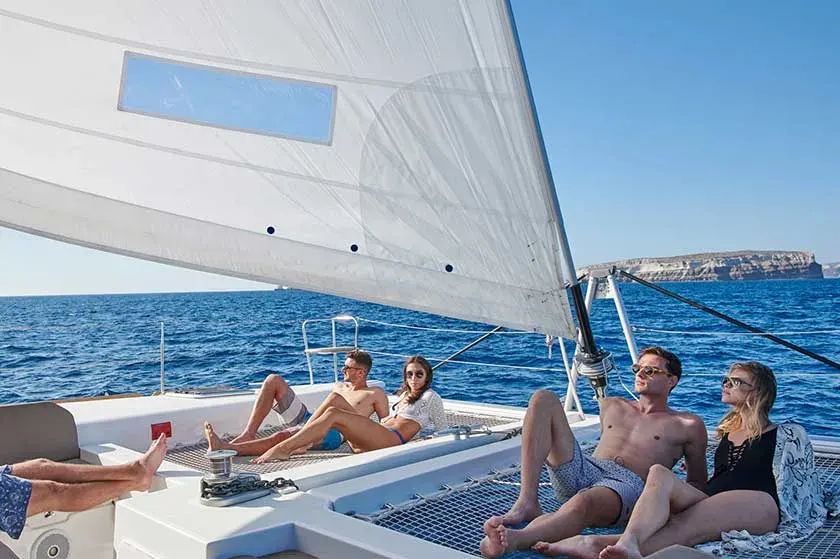 Friends relaxing under mainsail on sunset sailing tour