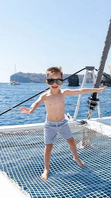 child balancing on catamaran trampoline during family cruise