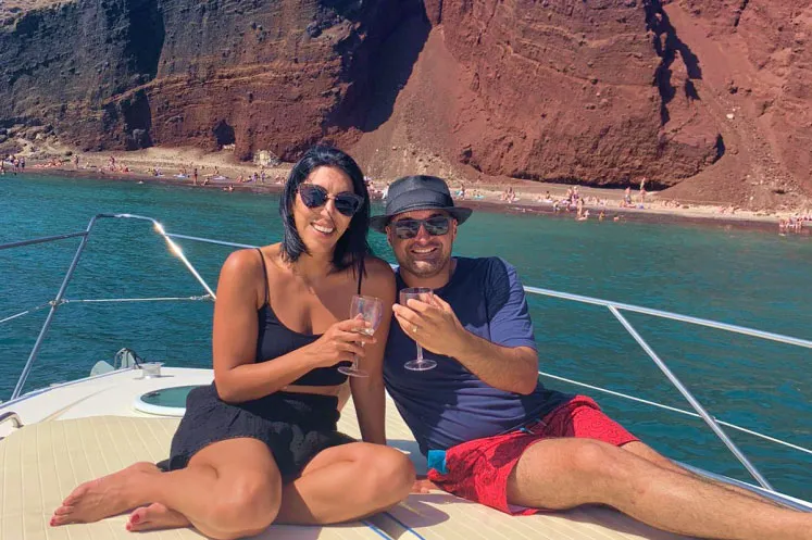 A couple on the deck of a catamaran in the Red Beach bay, with red cliffs behind them