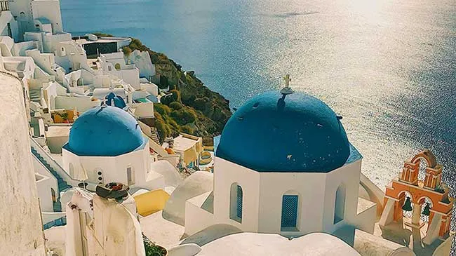 Blue-domed churches in Oia above the Santorini caldera, with the sea shining in the late sun