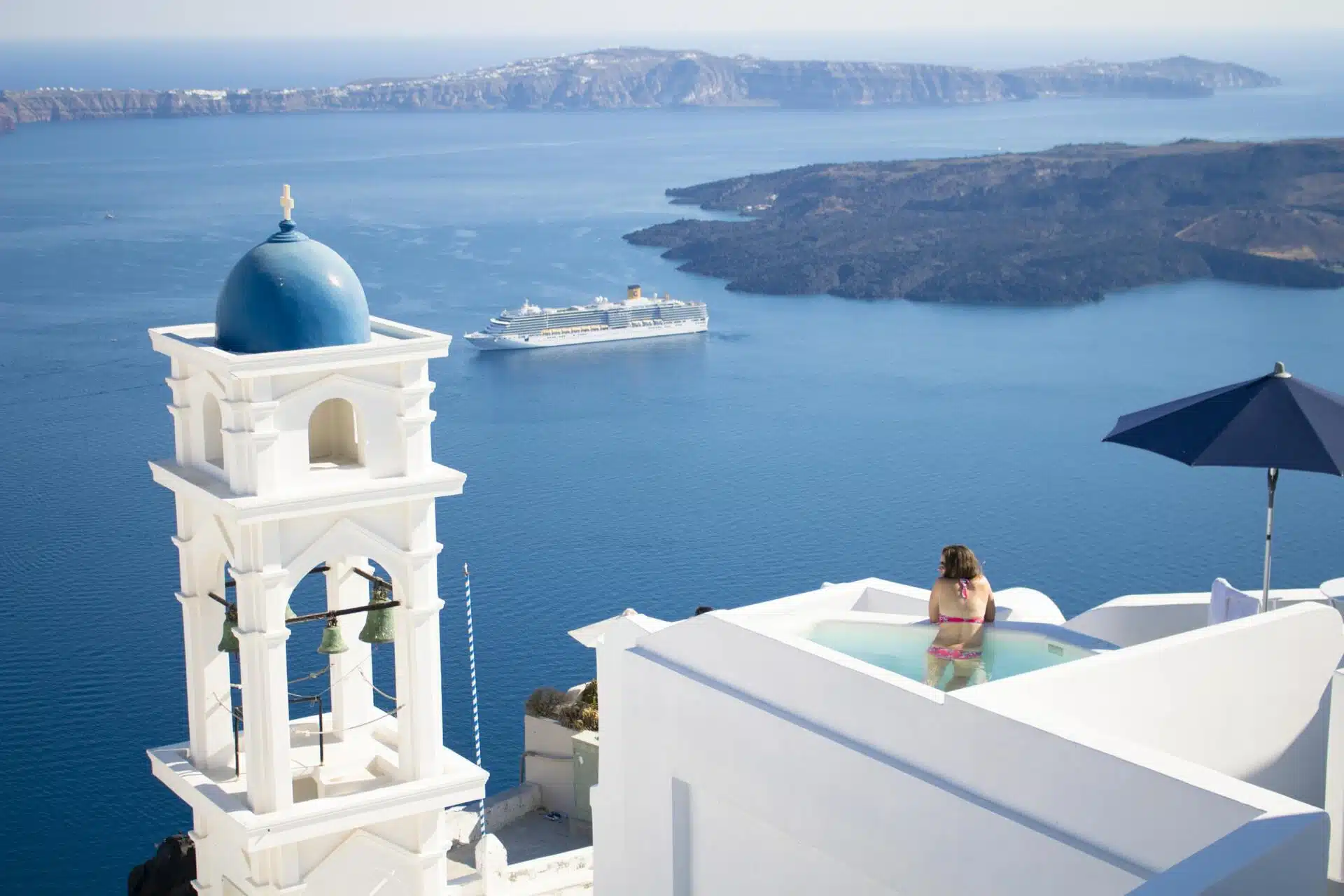 Blue-domed bell tower and a plunge pool above the Santorini caldera on a clear day