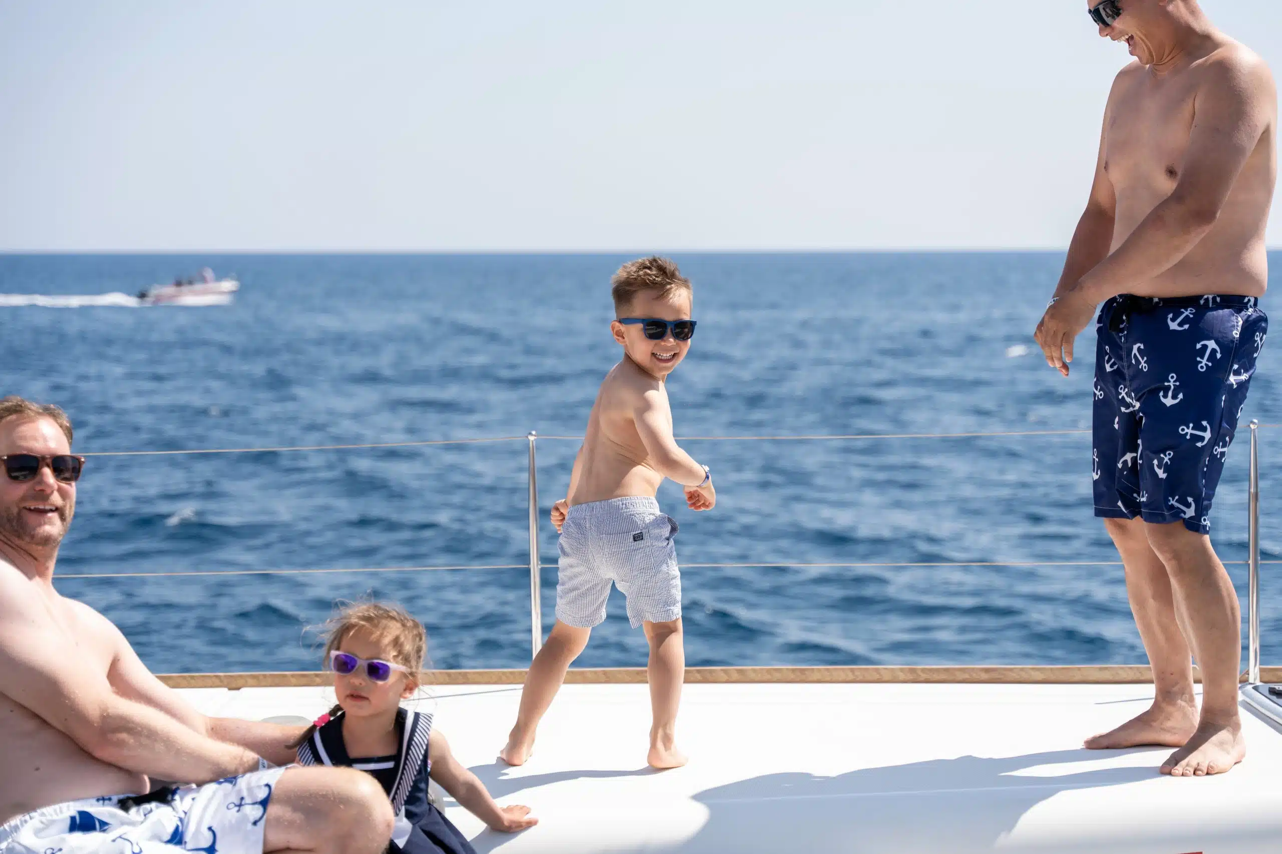 A family on the front deck of a catamaran, two children in sunglasses, with the open sea behind them
