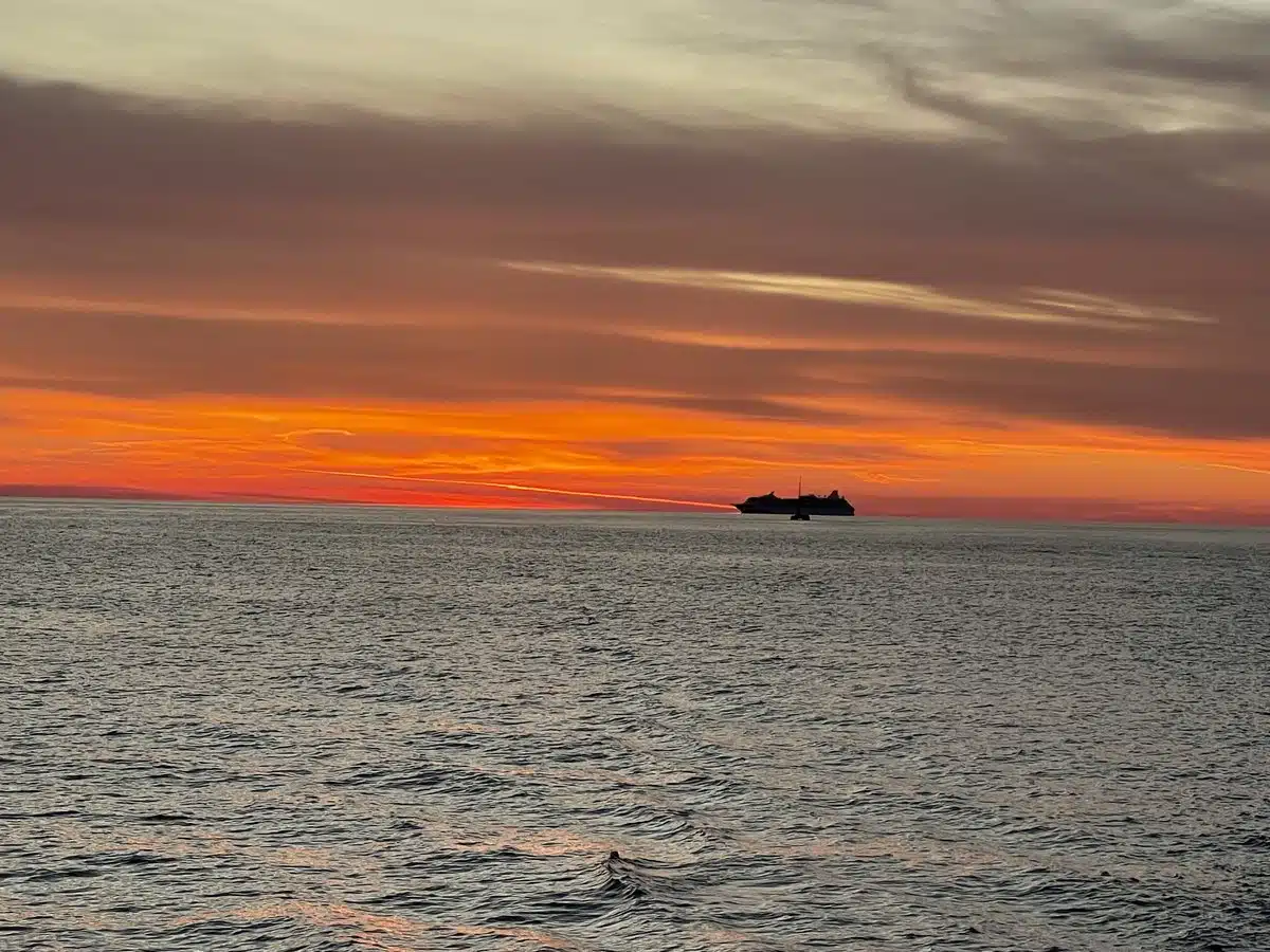 Sunset over the sea with a ship on the horizon, seen from a catamaran